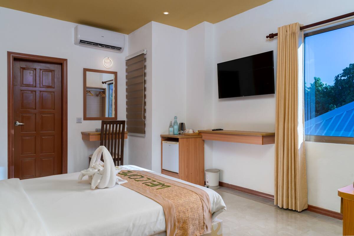 Habitación de hotel con cama, escritorio, televisor y ventana con cortinas.