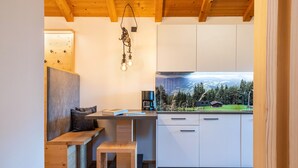 Eine moderne Küche mit Holzbalken, einer Bank, Blick auf einen Wald und einer Kaffeemaschine.
