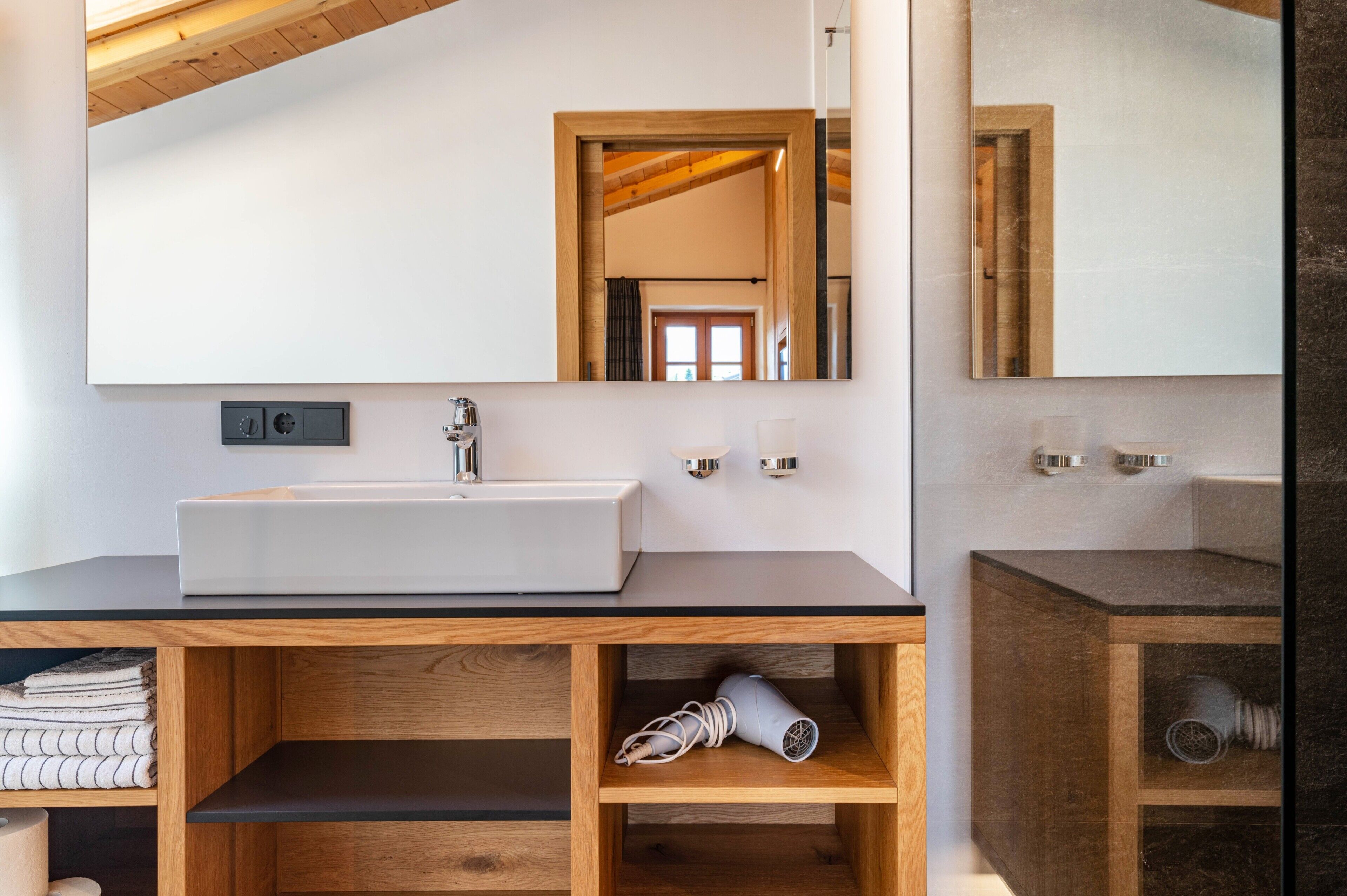A modern bathroom with a large mirror, a sink, and wooden shelves.