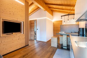 A modern kitchen with wooden beams, a built-in TV, and pendant lighting.
