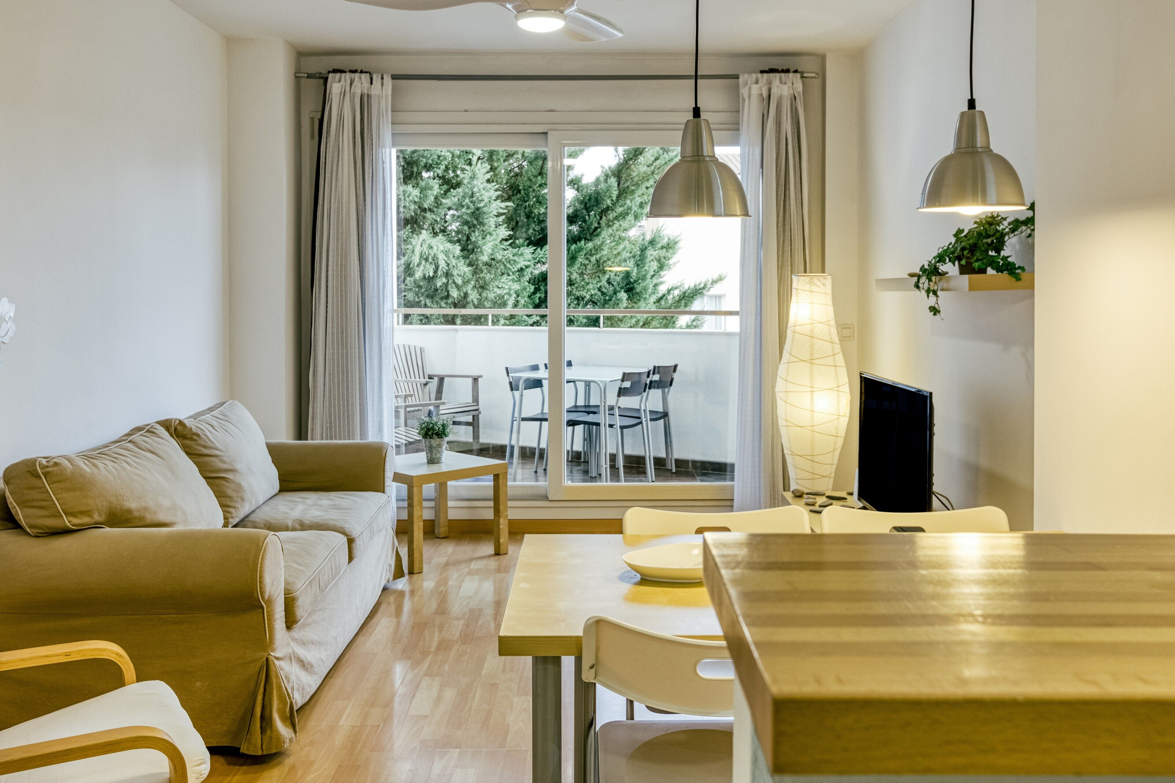 Ett modernt vardagsrum med en soffa, ett matbord, stolar, en tv och en balkong med utemöbler.