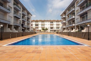A swimming pool with tiled flooring, surrounded by multi-story buildings with balconies and railings. - Apartment 'Omega 7' with Shared Pool, Shared Garden and Air Conditioning (L'Estartit)