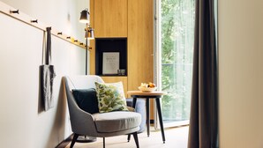 Quarto moderno com poltrona cinza, mesa redonda pequena com uma tigela de fruta, luminária de parede e um quadro emoldurado.