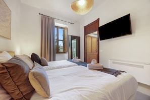 A hotel room with two beds, a flat-screen TV, a large window, and a ceiling light fixture.