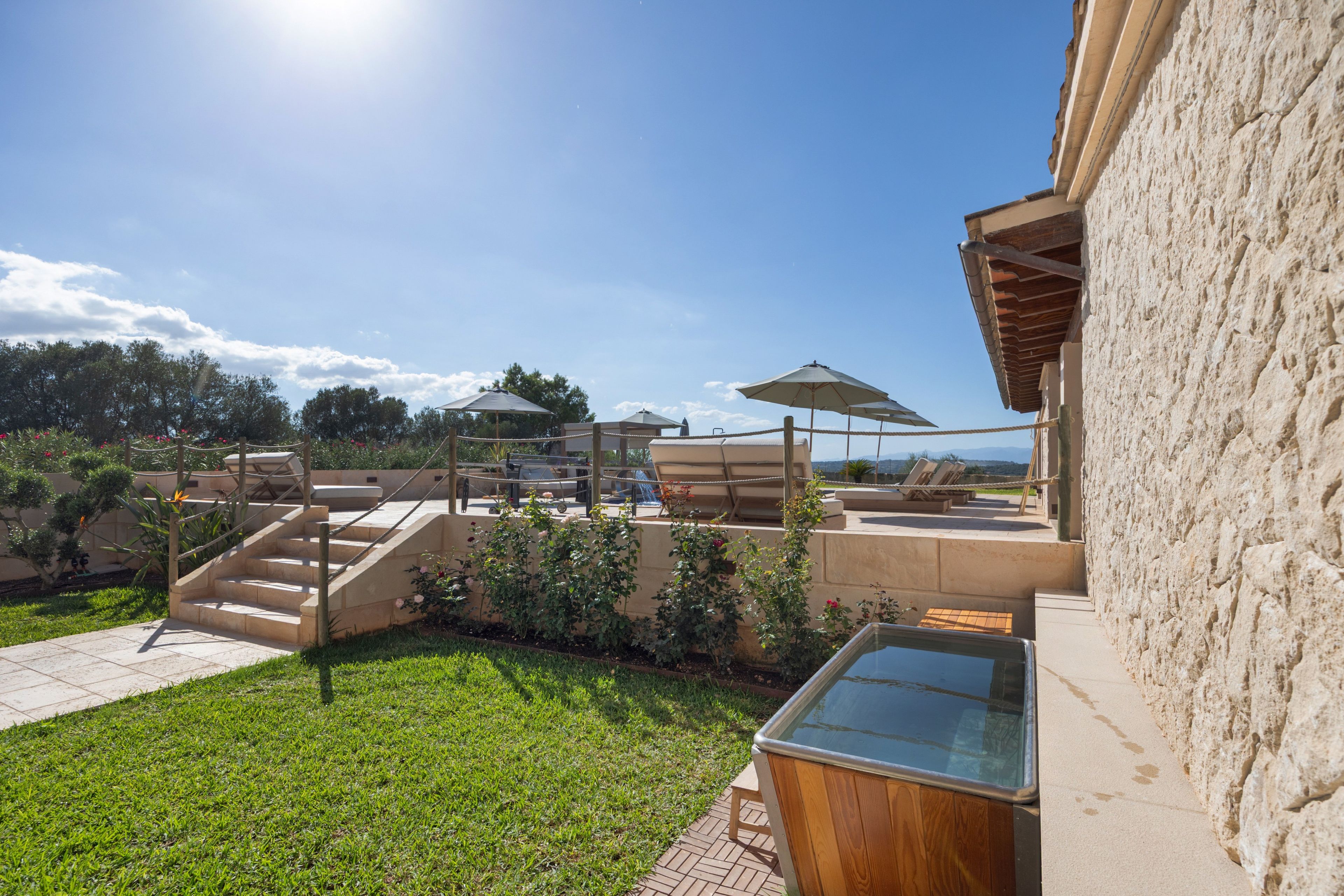 A pool area with steps leading down to the water, surrounded by greenery and a clear sky.
