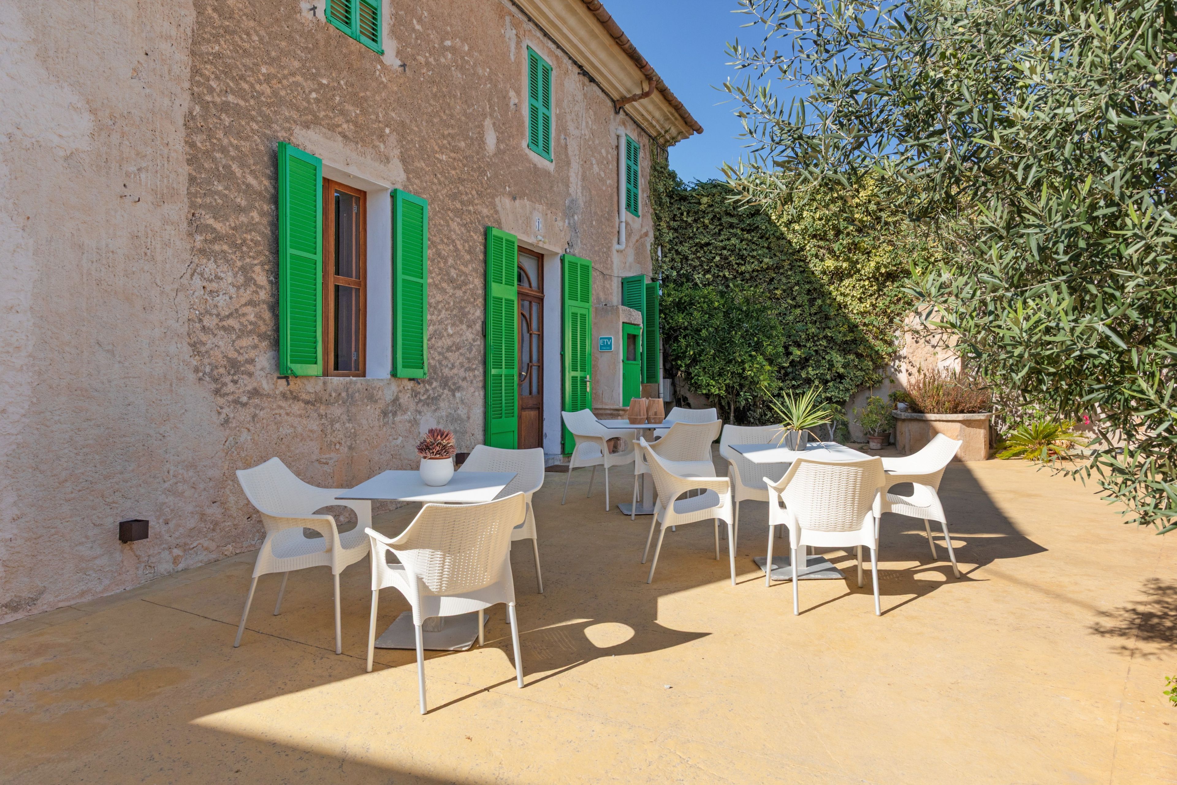 A building with green shutters and a patio with white chairs and tables.