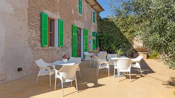 A building with green shutters and a patio with white chairs and tables.