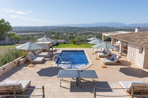 Un área de piscina en la azotea con sillones y sombrillas, con vistas a un paisaje pintoresco.