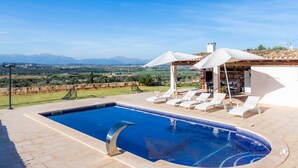 A swimming pool with lounge chairs and umbrellas, a view of the countryside, and a building with a chimney. - Vacation Home 'Sa Figuereta Living Place' with Mountain Views, Wi-Fi & Air Conditioning (ARIANY)