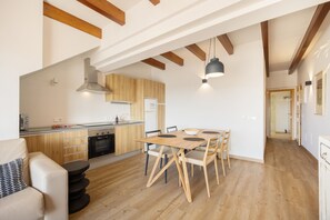 Una cocina moderna con armarios de madera, un comedor con mesa y sillas de madera, y una escalera que conduce a un nivel superior.