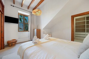 Ein Schlafzimmer mit einem Bett, einem Fernseher, einem Fenster mit Vorhängen und einer Holzbalkendecke.