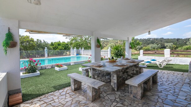 A covered patio with stone flooring, a stone table, and benches.
