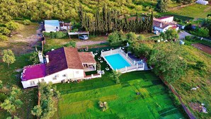 An aerial view of a property with a swimming pool, a large house, and surrounding green fields.