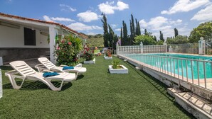 A pool area with artificial grass, white lounge chairs, and a white fence.