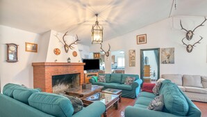 A living room with a brick fireplace, green sofas, and antler wall decorations.
