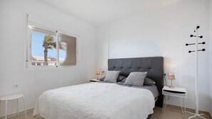 Quarto com cama grande, duas mesas de cabeceira, janela com vista e um abajur.