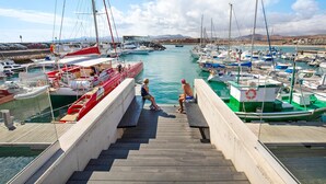Marina com barcos atracados, escadaria de madeira que desce até a água e vista distante de montanhas.