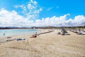 Ein Strand mit blauem Himmel, sandigem Ufer und einer entfernten Bergkette.
