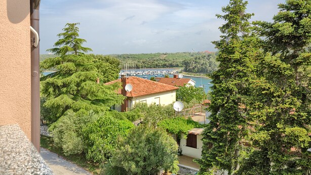 Una villa costera con vistas al mar, rodeada de vegetación exuberante y un puerto deportivo.