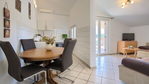 Una cocina moderna con armarios blancos, una mesa de comedor con sillas, un televisor sobre un mueble de madera y un balcón con una silla.