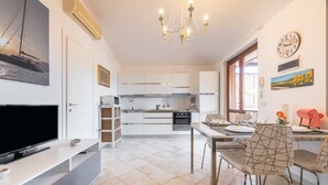 A modern kitchen with white cabinets, a dining area with a table and chairs, a TV, and artwork on the walls.