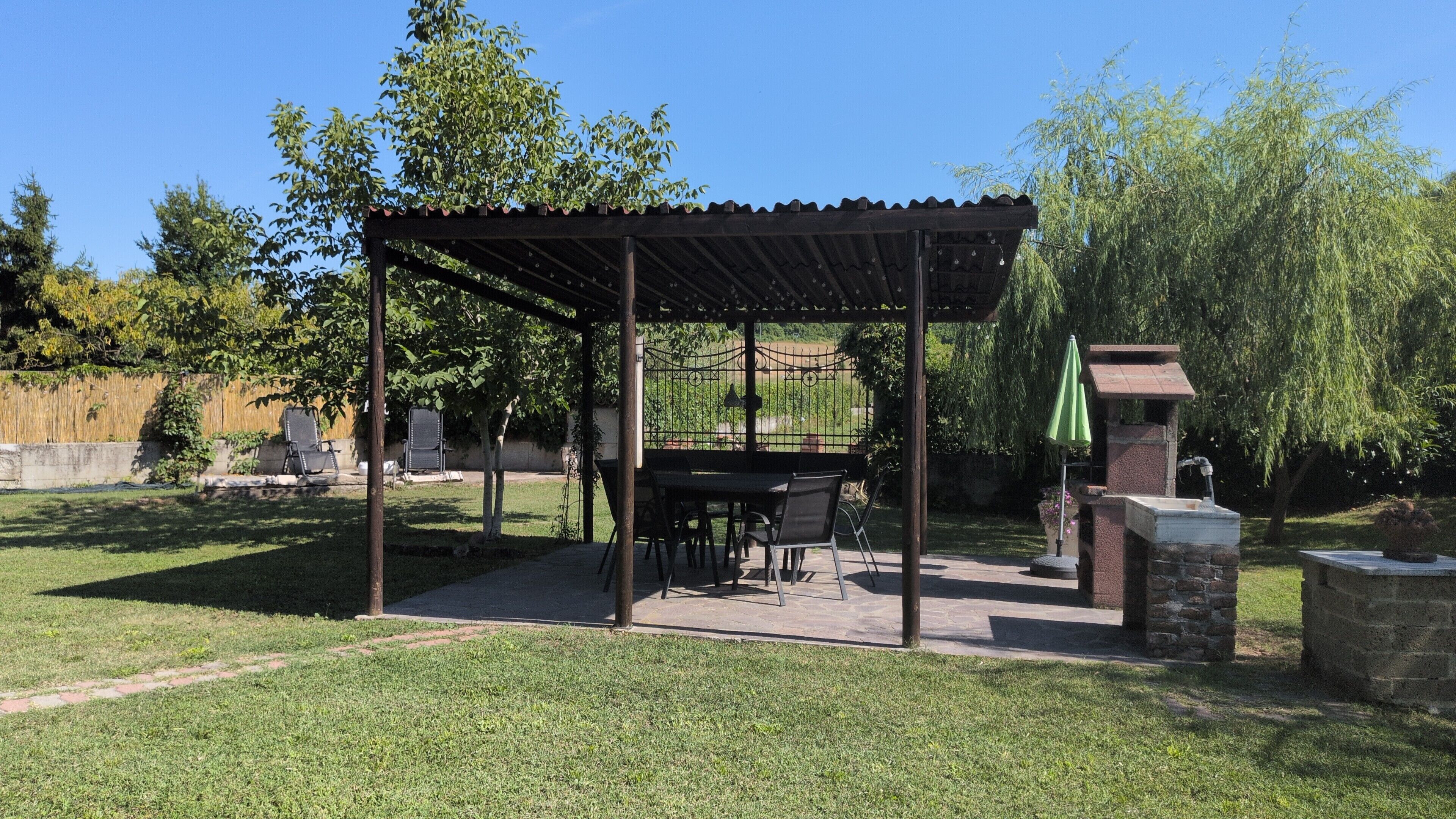 Een overdekt terras met een tafel, stoelen, een stenen constructie en een groene parasol.