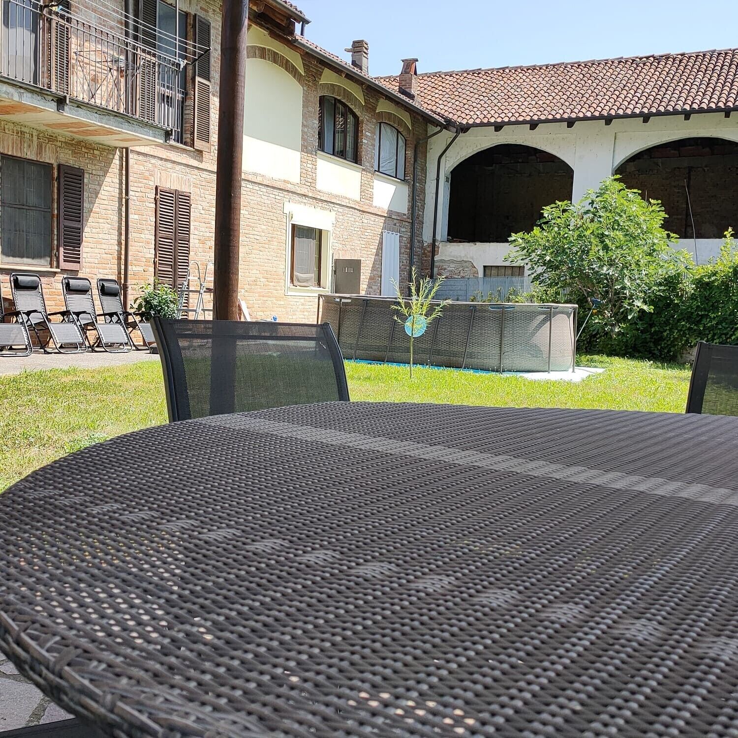 Eine Terrasse mit einem runden Tisch, Gartenstühlen und einem Gebäude mit Ziegeldach und Backsteinwänden.