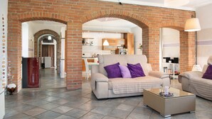 A living room with a brick archway, a sofa, a coffee table, and a kitchen in the background.