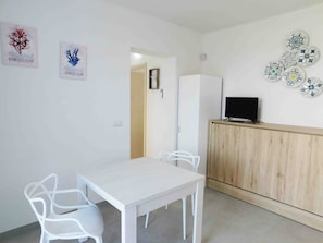 A room with a white table, white chairs, a TV on a wooden cabinet, and wall decorations including coral illustrations. - Apartment 'Bilo Vista Mare Dauni' with Balcony (Ugento)