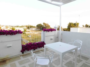 A balcony with a white table and chairs, a white railing, and purple flowers. - Apartment 'Bilo Vista Mare Dauni' with Balcony (Ugento)