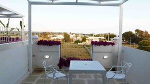 A balcony with a white table and chairs, a view of the city, and purple flowers on the railing.