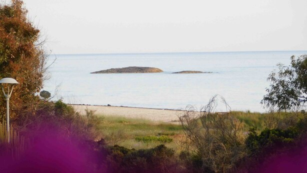 A beach with a rocky outcrop in the distance, a lamp post, and some vegetation in the foreground.