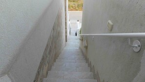 Eine schmale Treppe mit weißen Wänden und einem Metallgeländer, die zu einem Außenbereich führt.