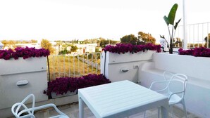 Ein Balkon mit weißen Möbeln, einem weißen Tisch und lila Blumen.