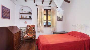 A bedroom with a bed, dresser, chair, and shelves with decorative items.