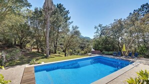 A swimming pool with a wooden deck, surrounded by trees and a mountain in the background. - Holiday Home 'Quinta La Rabide' with Mountain View, Wi-Fi and Air Conditioning (Azeitão)