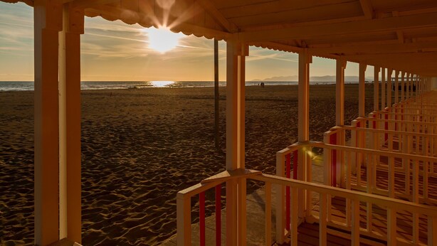 A beach view from a wooden structure with a railing, a clear sky, and the sun setting or rising.
