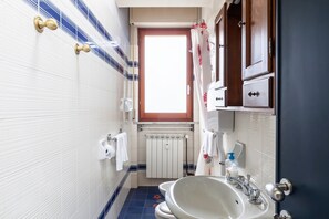 Casa de banho com lavatório branco, espelho, janela e radiador.