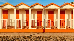 A row of beach huts with white and orange exteriors, wooden floors, and a clear blue sky.