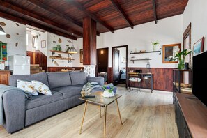 A living room with a sofa, coffee table, wooden flooring, and a kitchen area with a counter and shelves. - "Finca Viña Maria" with Sea View, Private Pool & Wi-Fi (Los Realejos)