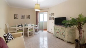 A living room with a sofa, dining table, chairs, a television, a cabinet, and a plant.