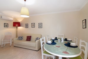 A dining area with a round table, white chairs, a sofa, a rocking chair, and a pendant light.