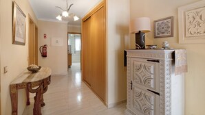 A hallway with a wooden door, a white cabinet with decorative panels, a table with a bowl, and a ceiling light fixture.