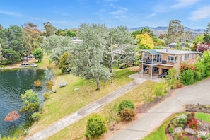 Une maison dotée d’un patio donnant sur un lac, entourée d’arbres et de collines.