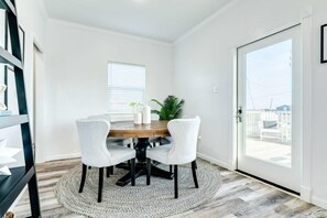 A dining area with a round wooden table, four white chairs, a small potted plant, and a window with blinds.