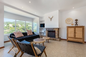 Una sala de estar moderna con un sofá, sillones, chimenea, televisión y vistas al exterior.