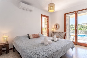 A bedroom with a bed, a bedside table, a lamp, a window, and a view of a swimming pool. - Villa 'Casa Escorpión' with Private Pool, Wi-Fi and Air Conditioning (Tossa de Mar)