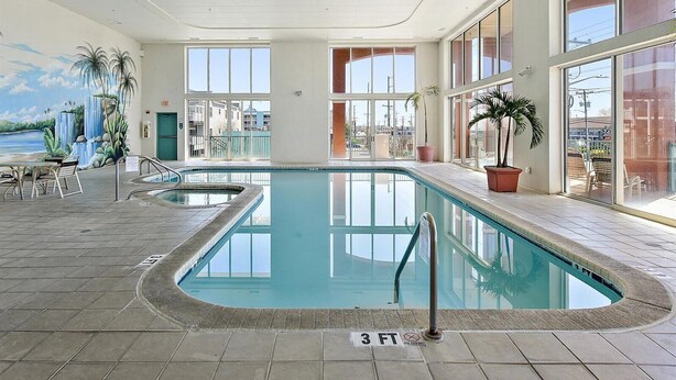 Una piscina interior con agua cristalina, un puesto de socorrista y vistas a la ciudad a través de amplios ventanales.