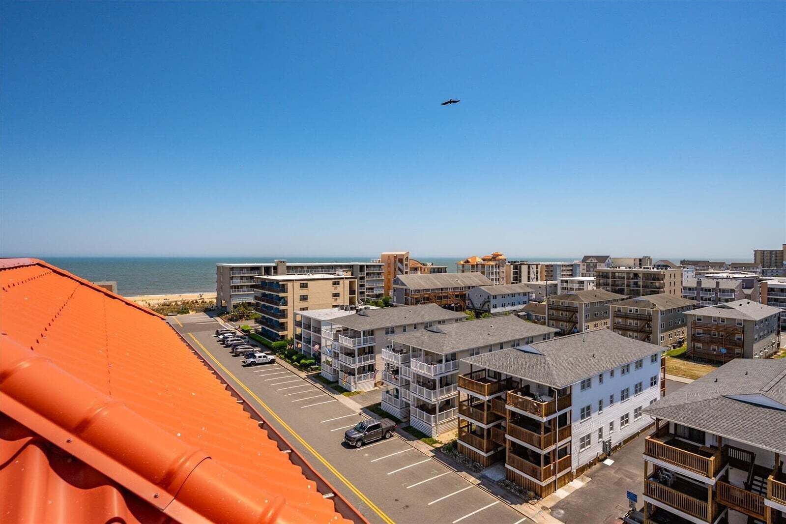 A coastal hotel with multiple-story buildings, a parking lot, and a view of the beach and ocean.