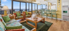 Un vaste espace de vie avec balcon, des meubles en bois et une cuisine équipée d’appareils électroménagers blancs.